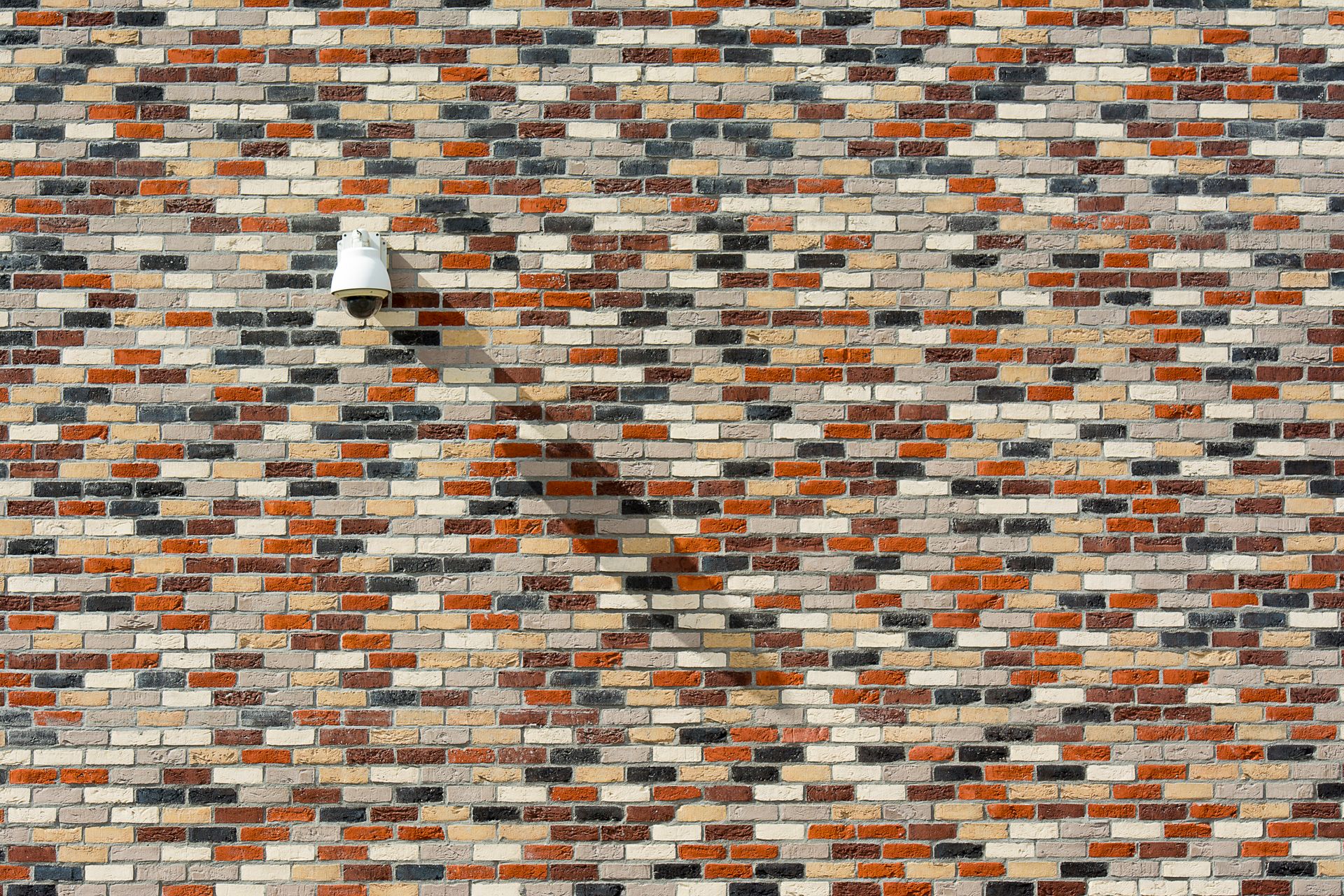 A vibrant brick wall with a security camera casting a shadow under sunlight.