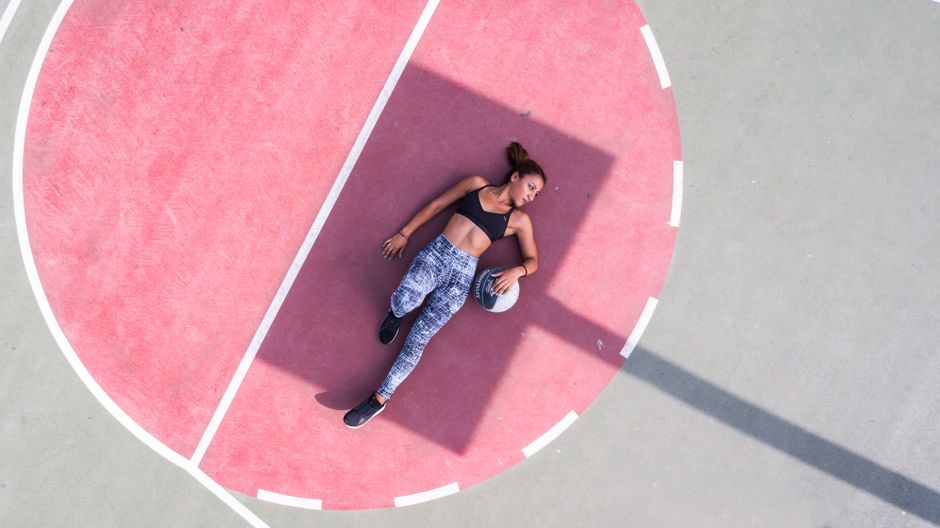Aerial shot of a woman lying on a basketball court holding a ball, enjoying leisure time.