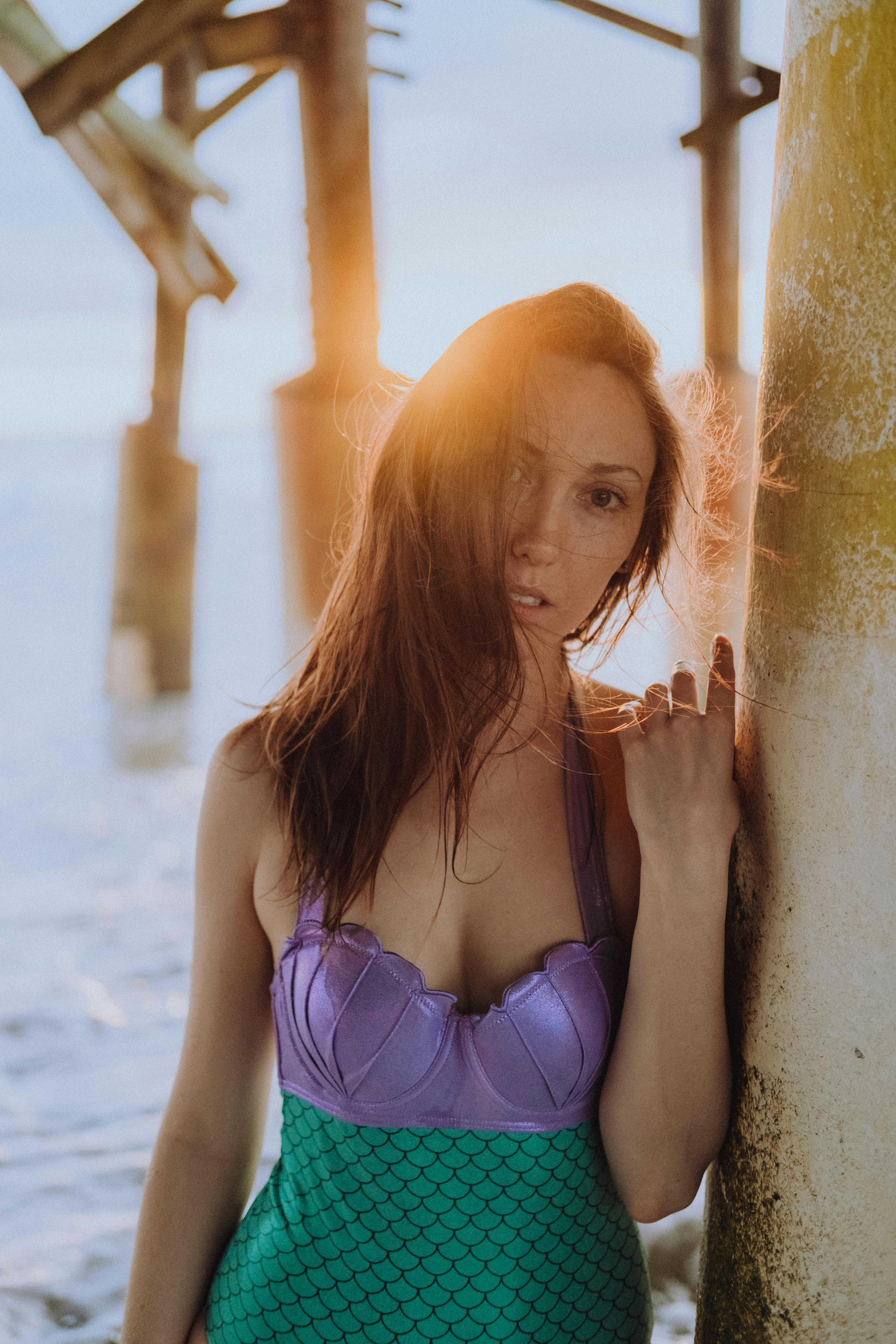 Woman in mermaid swimsuit at the beach during sunset, creating a magical ambiance.