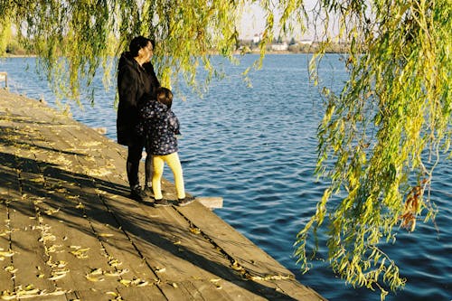 Woman and Child Standing on Wooden Dock Near Water