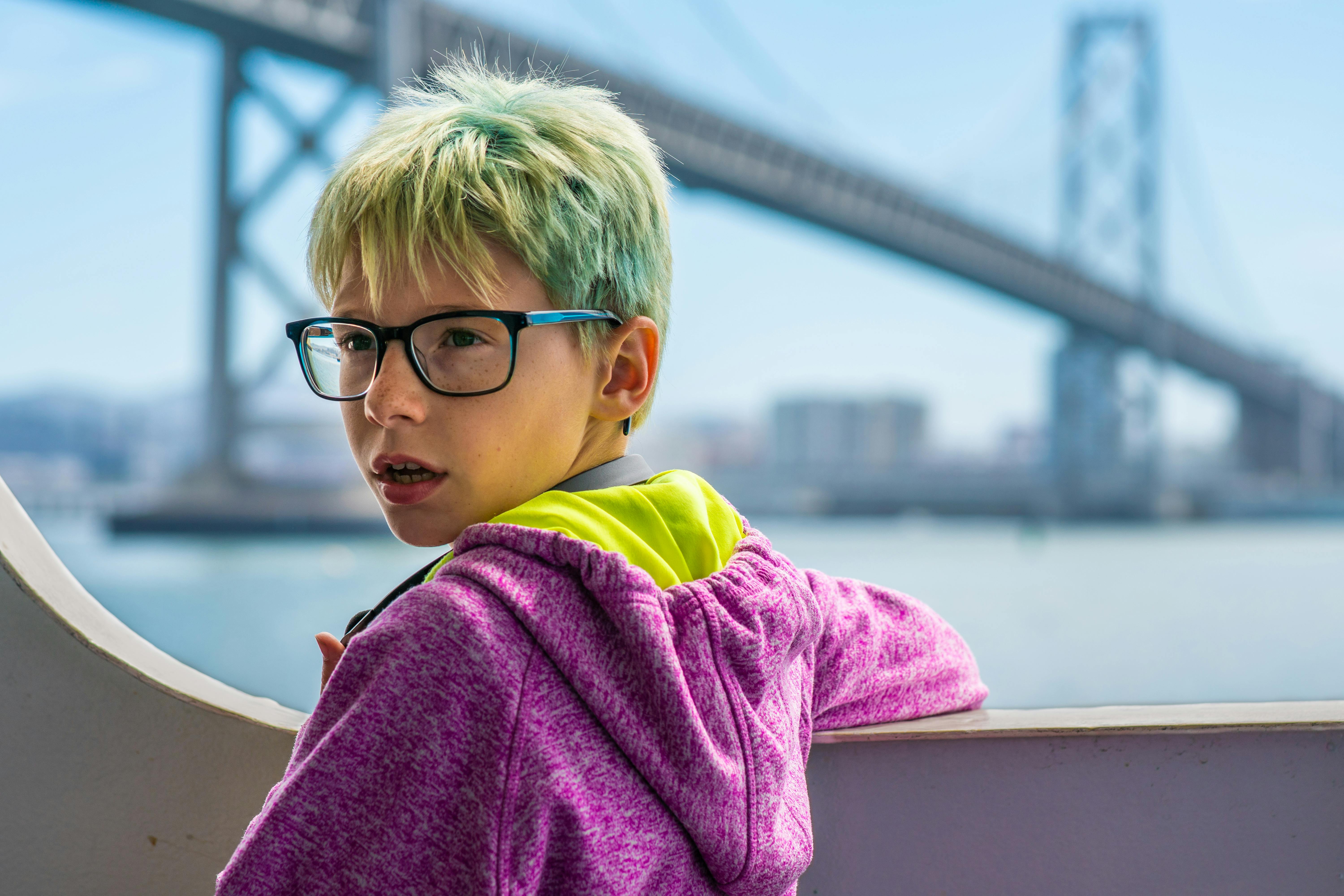 阳光明媚的一天，一个戴着眼镜的小男孩站在一座著名的桥附近