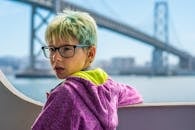 阳光明媚的一天，一个戴着眼镜的小男孩站在一座著名的桥附近