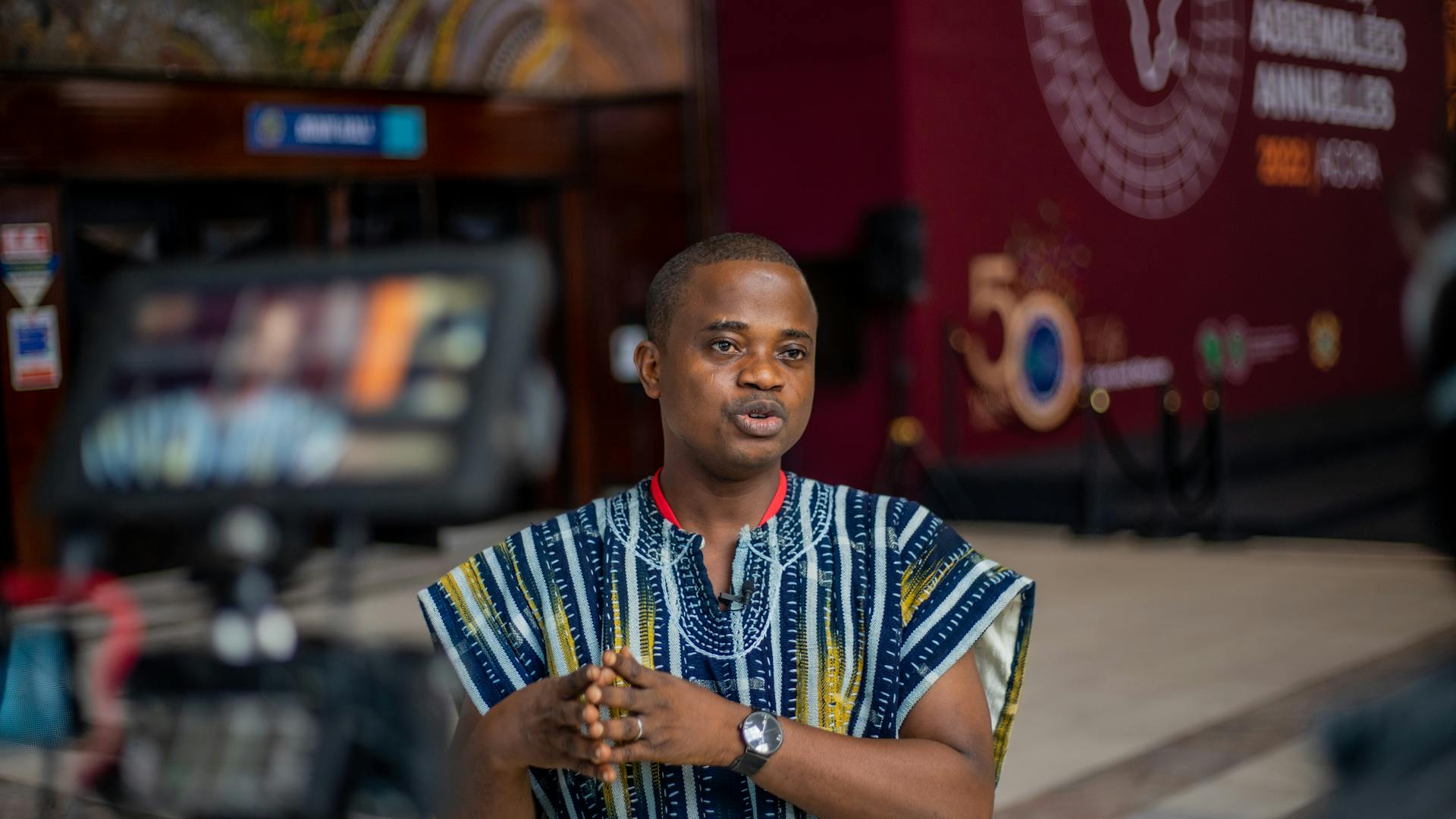 A man in traditional Ghanaian smock giving an interview at an event in Obuasi.