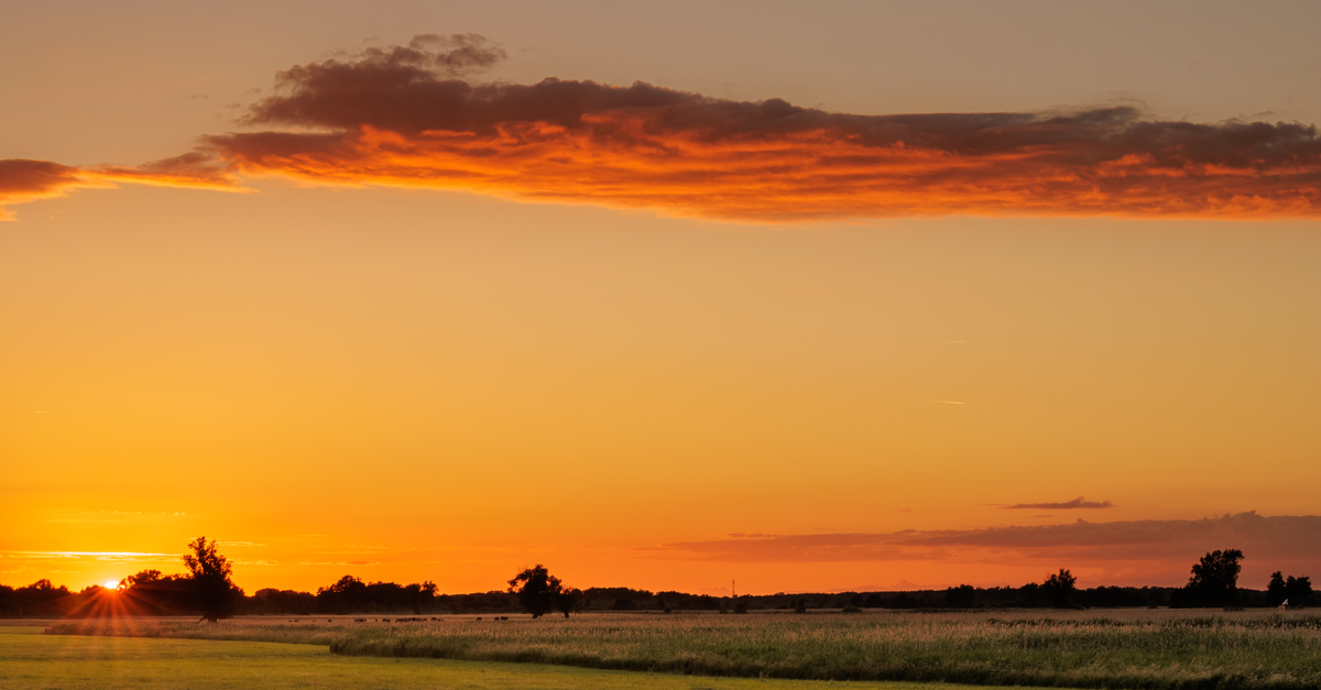 sunset sky with light breaking through clouds over a calm landscape