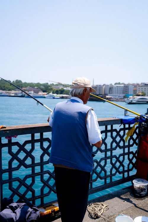 Free Senior man enjoying fishing on a sunny day at a city pier overlooking the water. Stock Photo