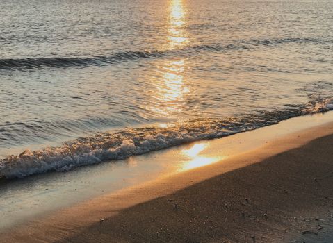 Golden sunset reflecting on waves at a tranquil beach, perfect for nature and travel imagery.