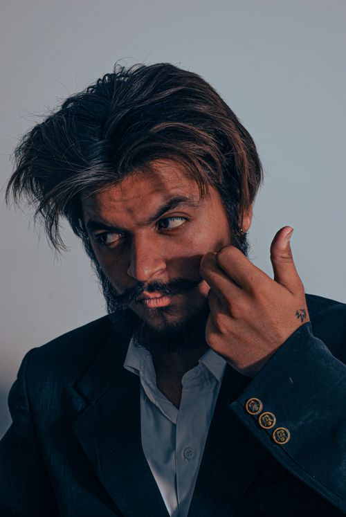 Free Elegant portrait of a bearded man in a blazer adjusting his mustache. Perfect for fashion and lifestyle themes. Stock Photo