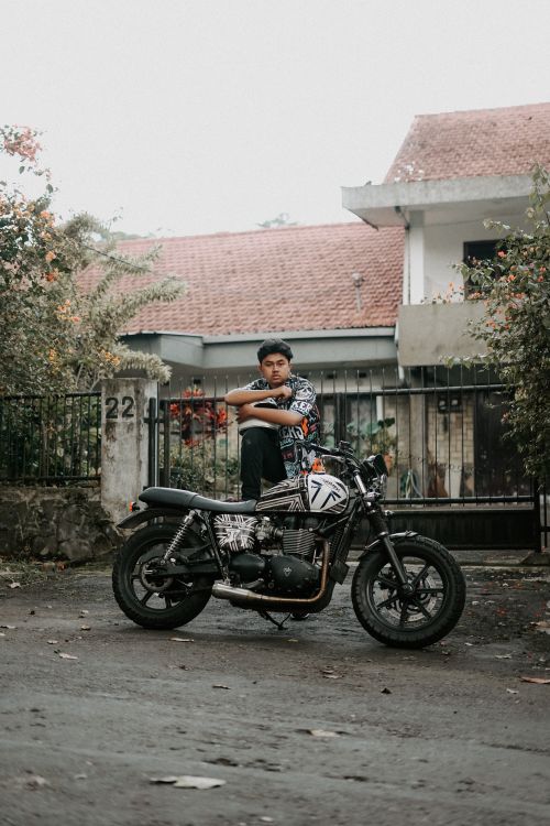 Free A man stands confidently with his classic motorcycle in a suburban outdoor setting. Stock Photo