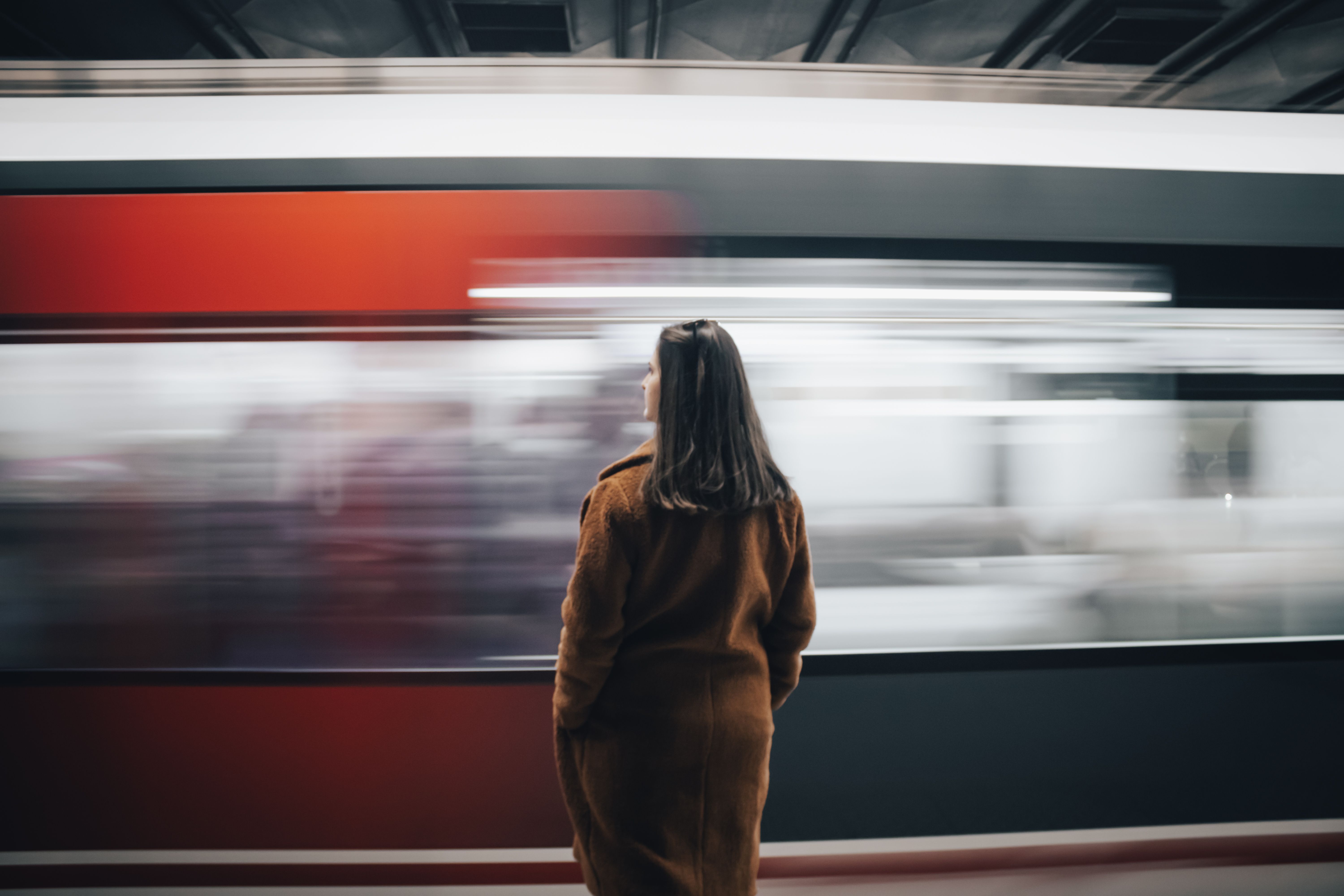 A woman in a brown coat stands on a subway platform as a train speeds by in İzmir, Turkey.