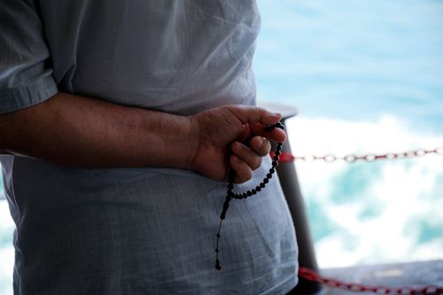 Free A person holds prayer beads while reflecting by the water, symbolizing spirituality and calm. Stock Photo