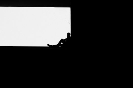 Minimalist silhouette of a man sitting alone in a stark black and white composition.