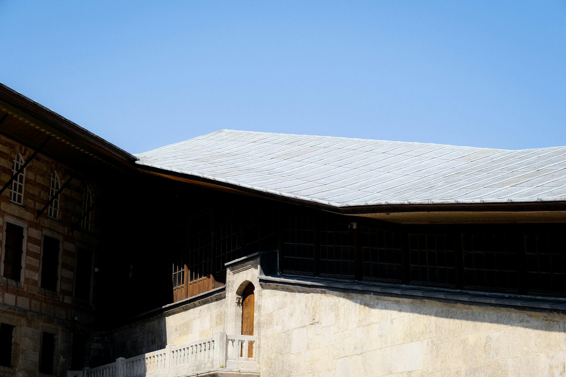 Exterior shot of a historic stone building featuring wooden windows and a gabled roof under a clear blue sky.