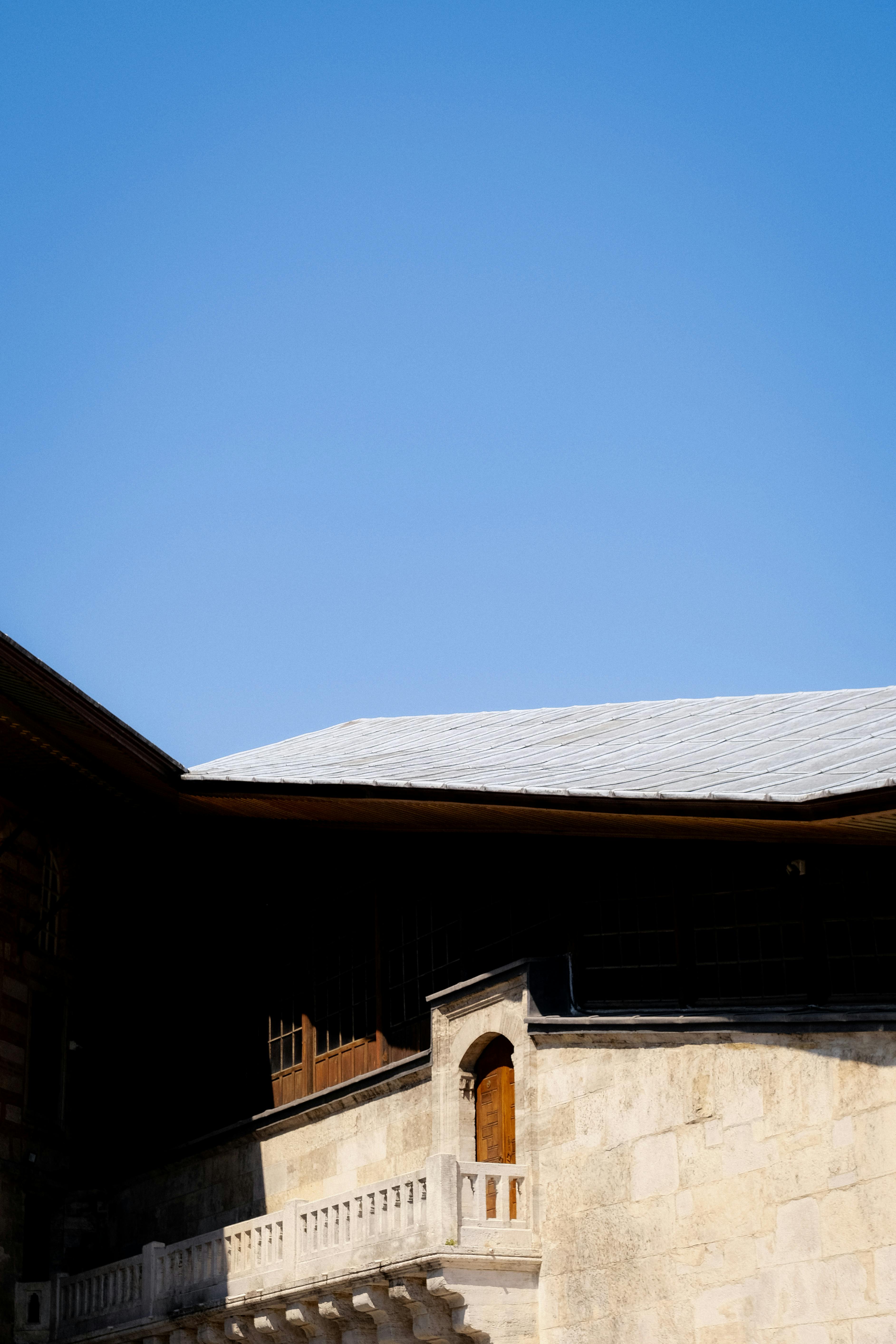 A classic stone building with a wooden door and a prominent roof under a clear blue sky.