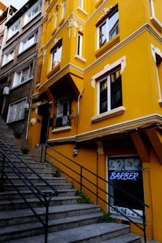 A striking urban scene of a vibrant yellow building with a neon barber sign, next to an outdoor staircase.