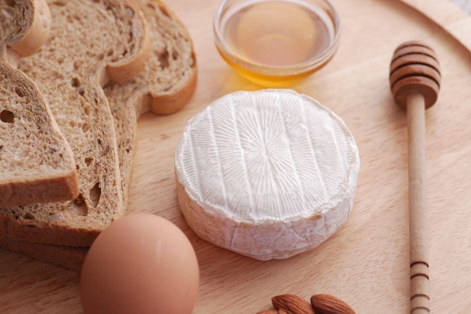 A whole round of Camembert in its wooden box, rind bloomy and pale, with a wedge cut out showing the soft, oozing interior.