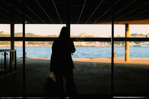 Free Silhouette of a person standing at a glass window with a view of the cityscape and body of water. Stock Photo