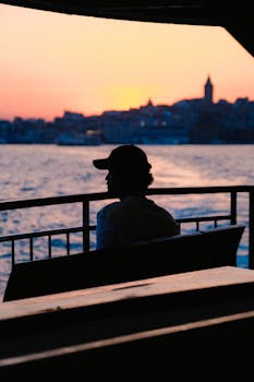 Silhouette of a man seated on a bench by the sea during sunset, creating a serene atmosphere.
