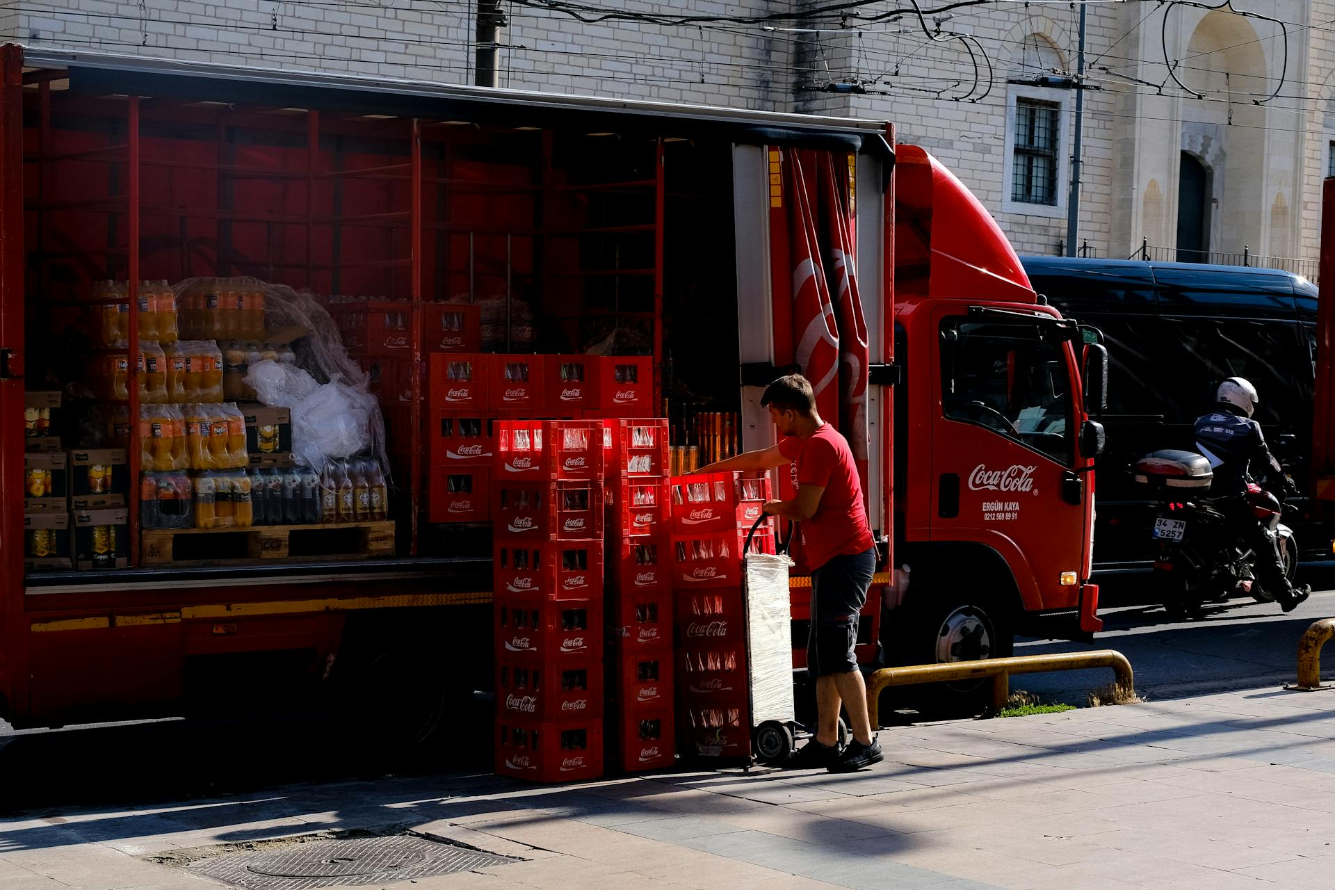 Delivery worker unloading Coca Cola crates from truck on city street, showcasing beverage supply logistics.