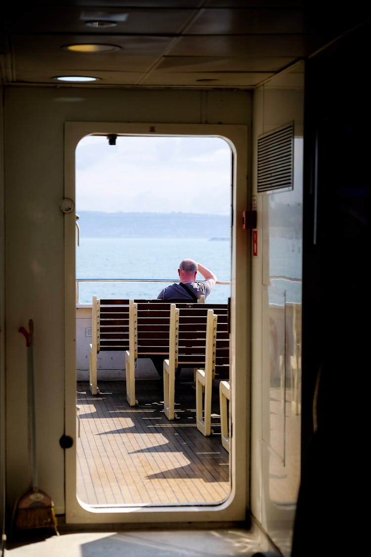 Photo Of A Man Sitting On The Bench On A Ship Deck