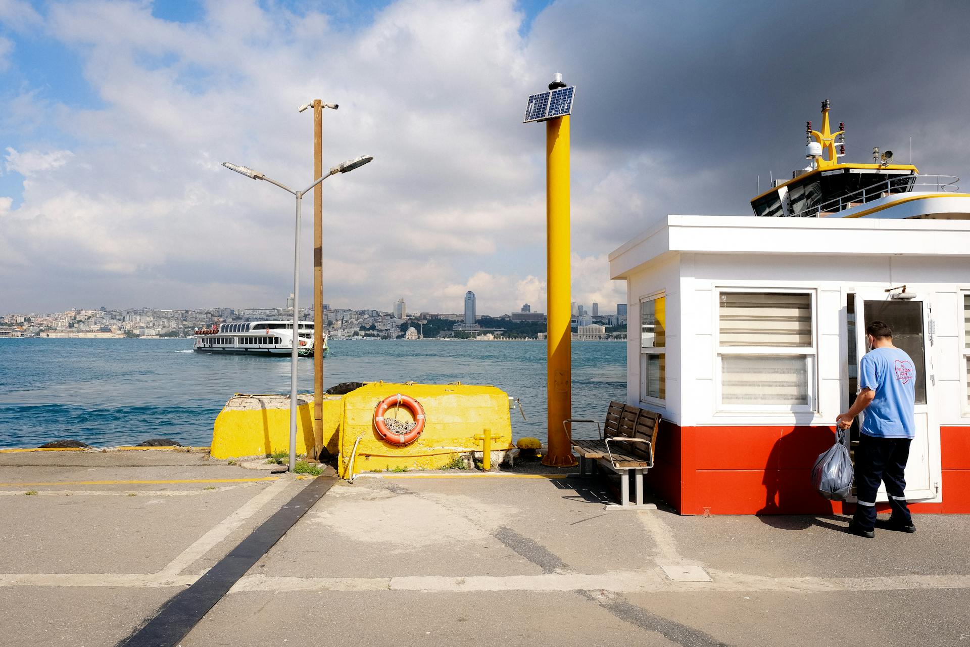 A picturesque scene at an Istanbul ferry terminal with a ferry in the harbor and a worker entering a booth.
