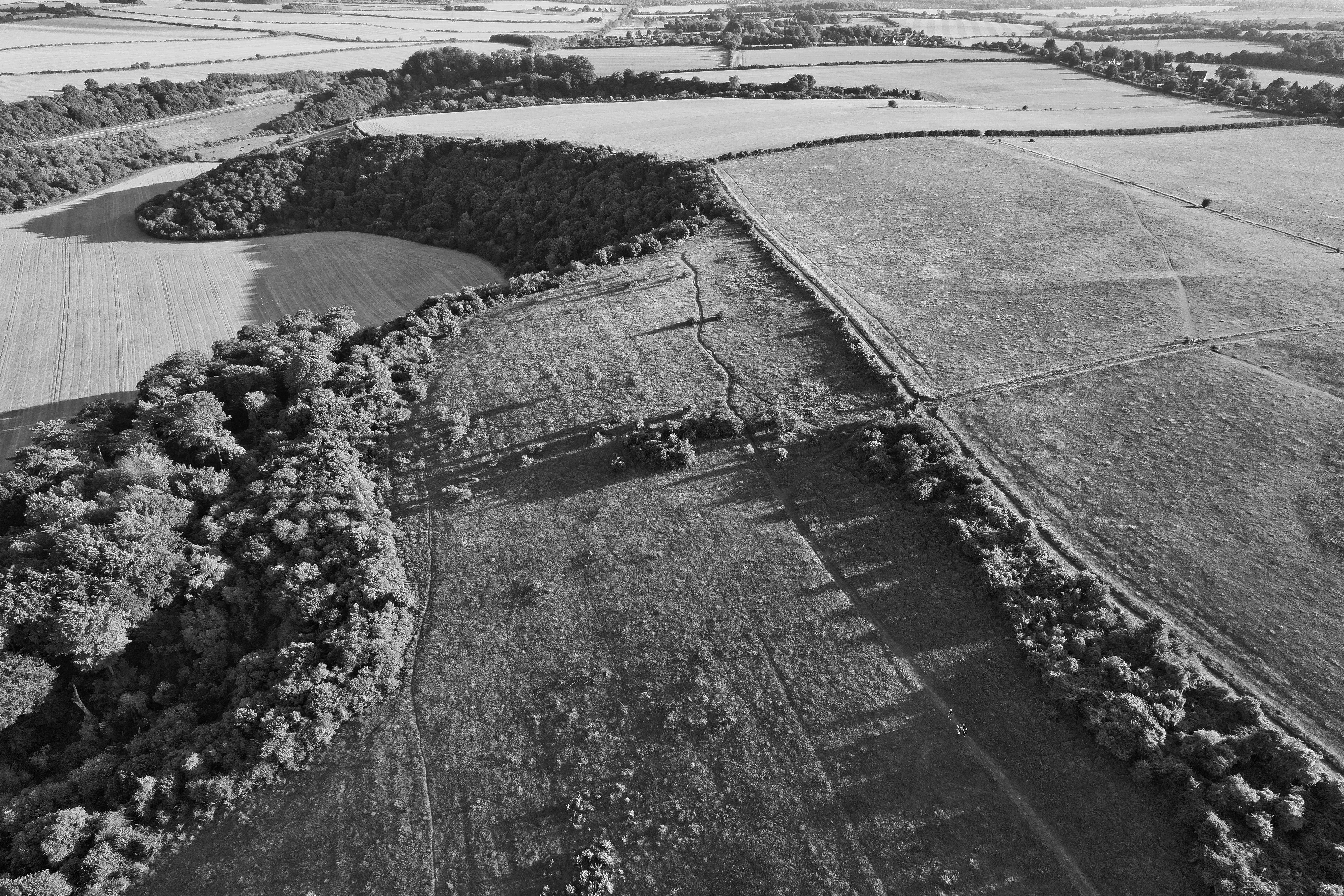 Black and white aerial view of rural countryside farmland in England showing fields and woodlands.