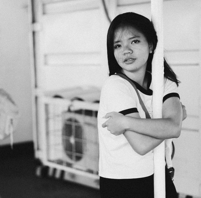 Black and white photo of a young woman hugging a pole indoors.