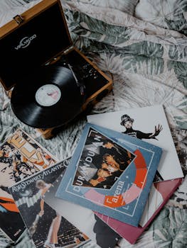 A collection of classic vinyl records and a retro record player on a cozy bed.