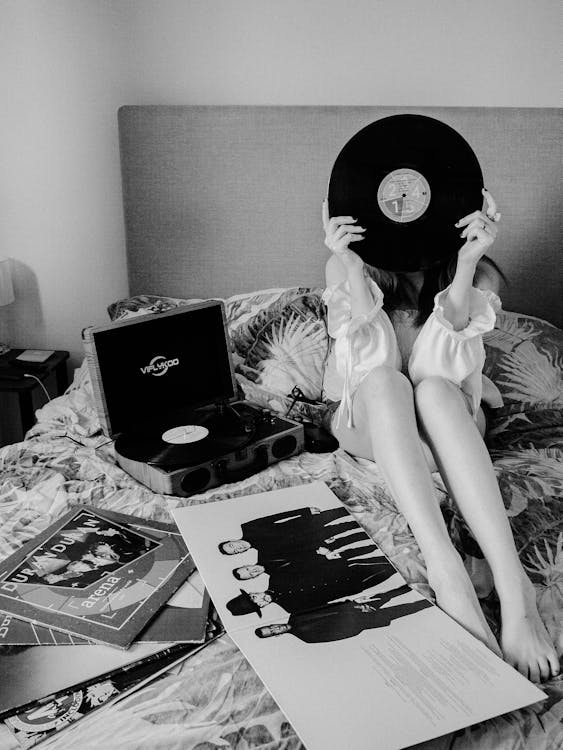 Free Woman Sitting on Bad and Holding Vinyl Record  Stock Photo