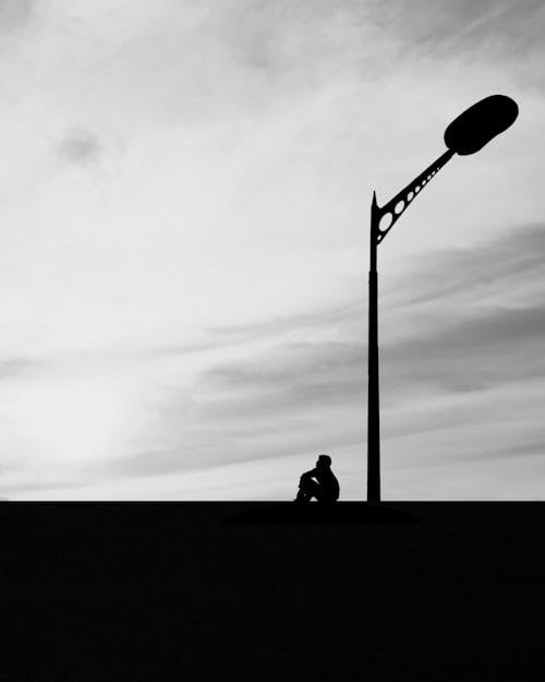 Silhouette of Person Sitting Near Light Post 