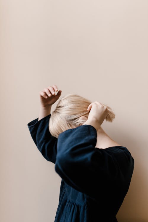 Blond Woman Fixing Hair Against Beige Wall