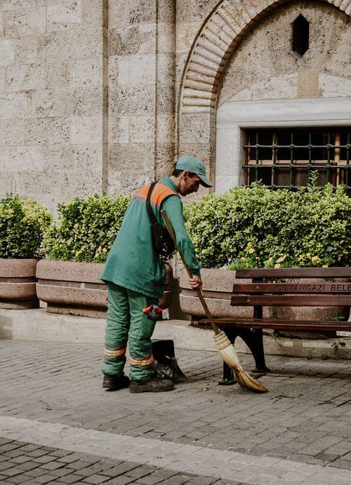 Free A street worker sweeps a park path in Turkey, wearing green uniform near leafy bushes. Stock Photo