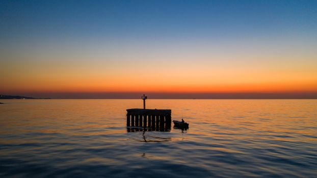Peaceful sunset view with a lone boat beside a pier on tranquil waters in Yalova, Turkey.