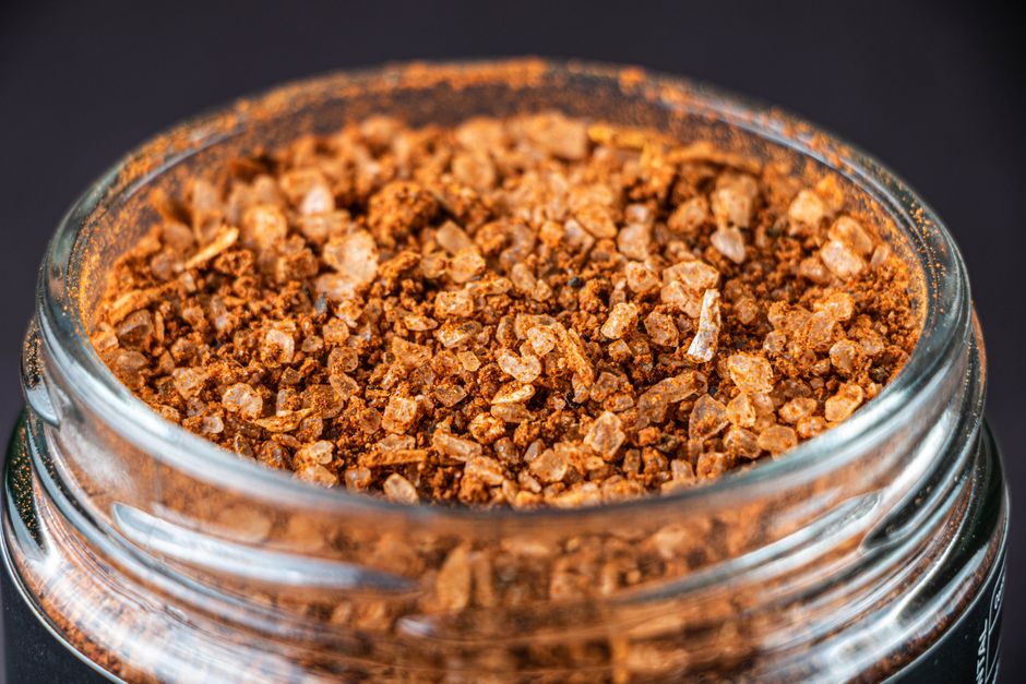 A small glass jar filled with a tan, flaky homemade onion soup mix blend of dried minced onion and bouillon granules, with a wooden spoon and loose dried onion flakes scattered beside it.