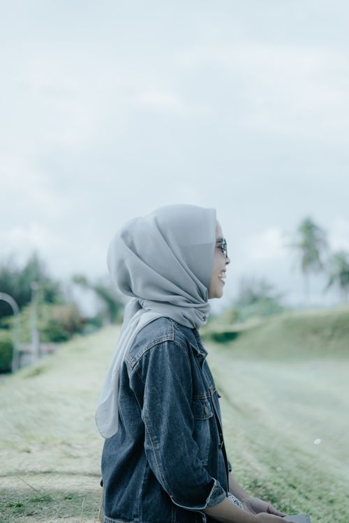Free Woman wearing hijab and denim jacket smiling joyfully in a serene outdoor setting. Stock Photo