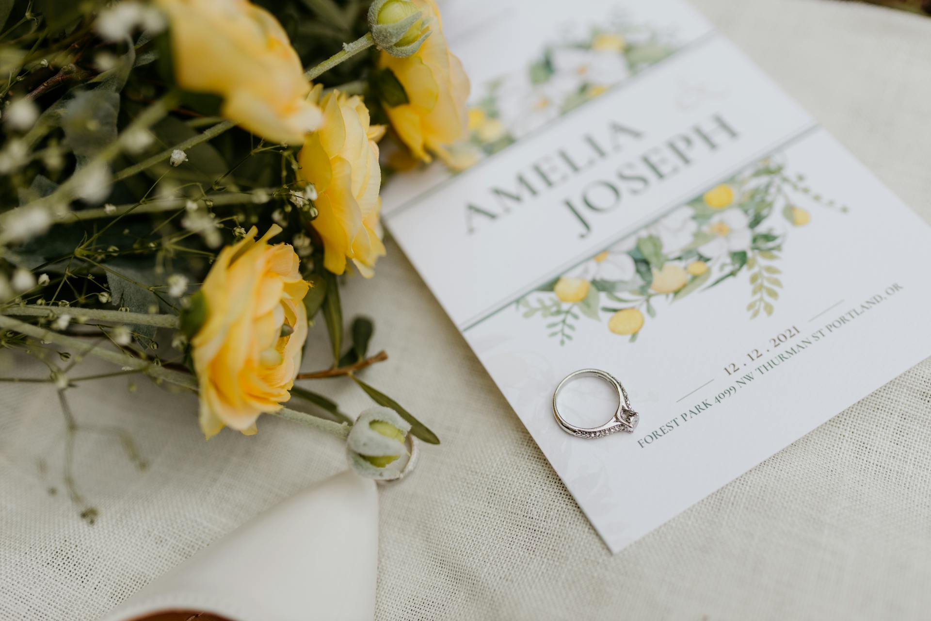 Close-up of wedding invitation adorned with yellow flowers and engagement ring, perfect for elegant wedding themed designs.