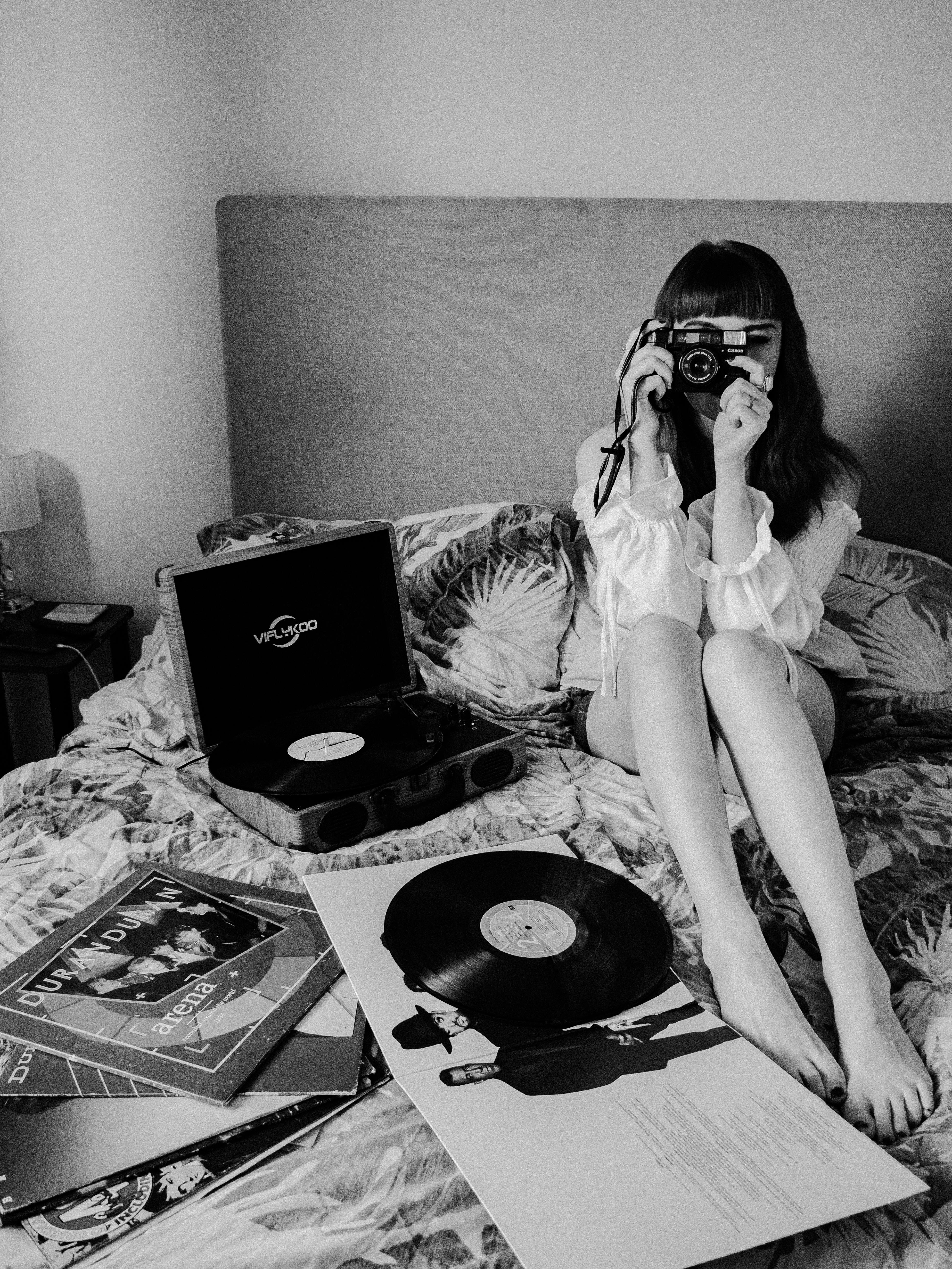 A young woman sitting on a bed capturing a moment with a vintage camera surrounded by vinyl records.