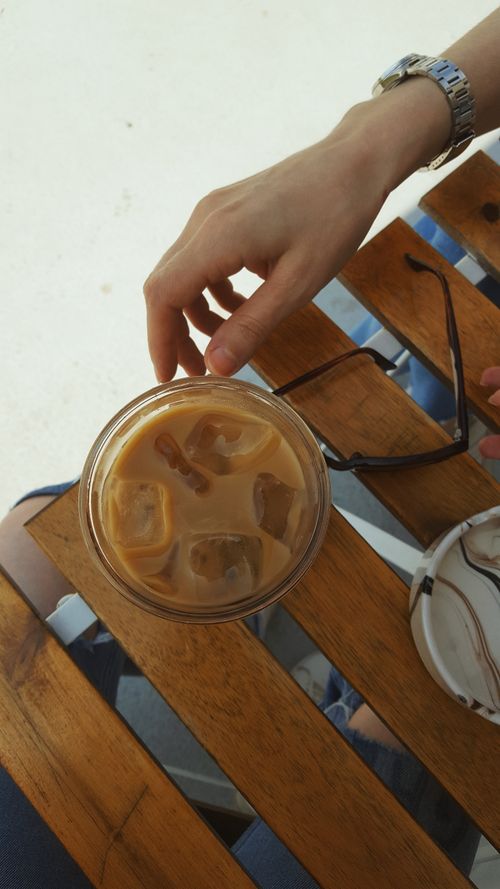 Free Overhead view of a hand holding iced coffee on a wooden table outdoors. Stock Photo