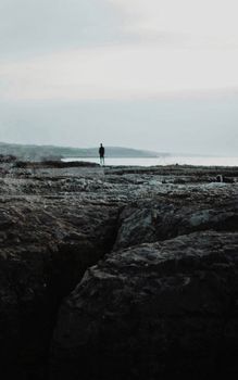 Calm coastal scene in Kocaeli, Türkiye, with solitary figure on rocky shore under overcast skies.