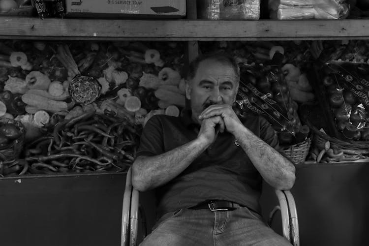 A Grayscale Photo Of An Elderly Man Sitting On The Chair