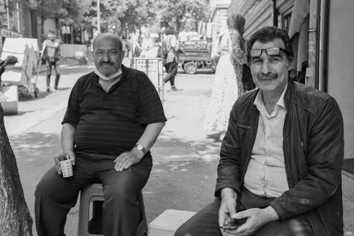 A Grayscale Photo of an Elderly Men Sitting on the Street