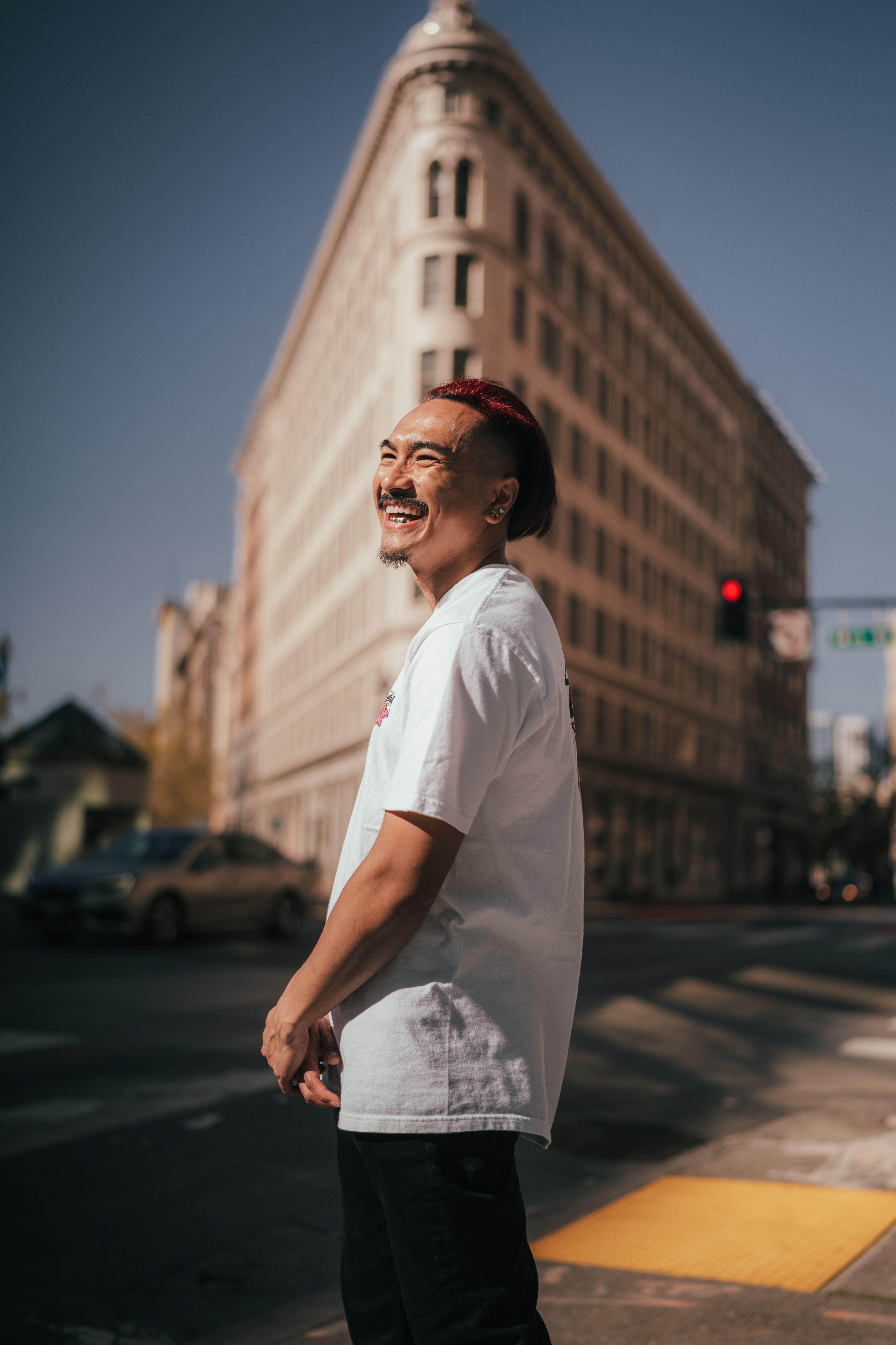 An Asian man smiling in front of a historic building in Oakland, California, embracing urban street style.