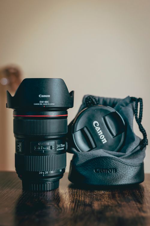 Free Close-up of a Canon camera lens with pouch on a wooden table, perfect for photography enthusiasts. Stock Photo