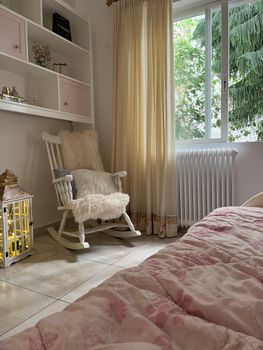 Inviting bedroom corner with a rocking chair, soft textiles, and garden view.