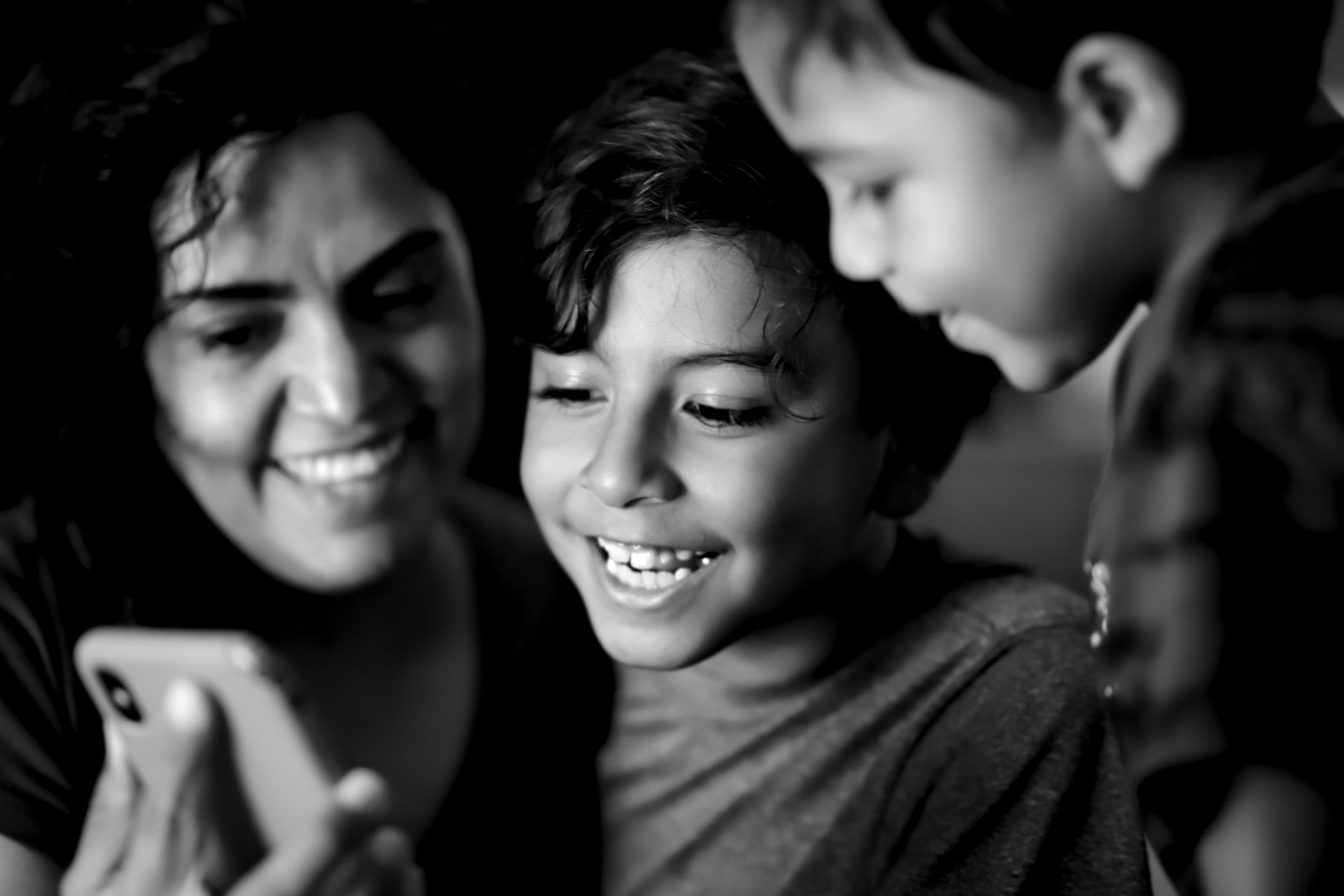 A joyful family moment with children and woman smiling at a phone screen, in black and white.