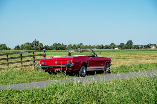 A classic red convertible parked in a lush rural landscape on a sunny day.