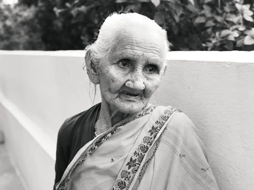 Free A Grayscale Photo of an Elderly Woman Near the Concrete Wall Stock Photo