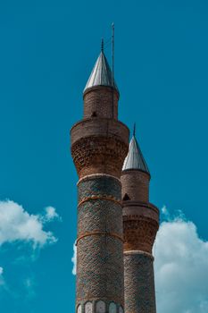 View of the historic twin minarets of a landmark mosque in Sivas, Türkiye, under a blue sky.