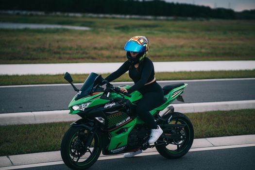 Confident woman rides a Kawasaki Ninja on a quiet road, emphasizing safety gear.