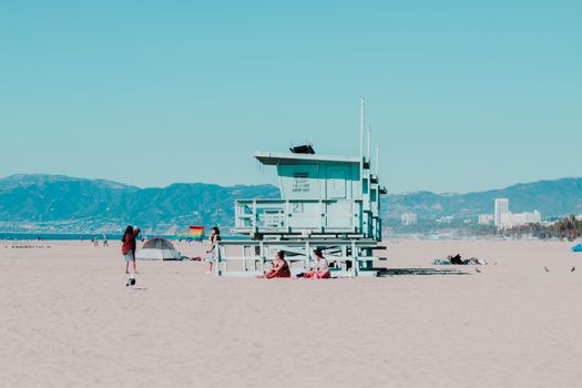 Sunny day at Santa Monica Beach featuring a lifeguard tower and beachgoers with a mountain view.
