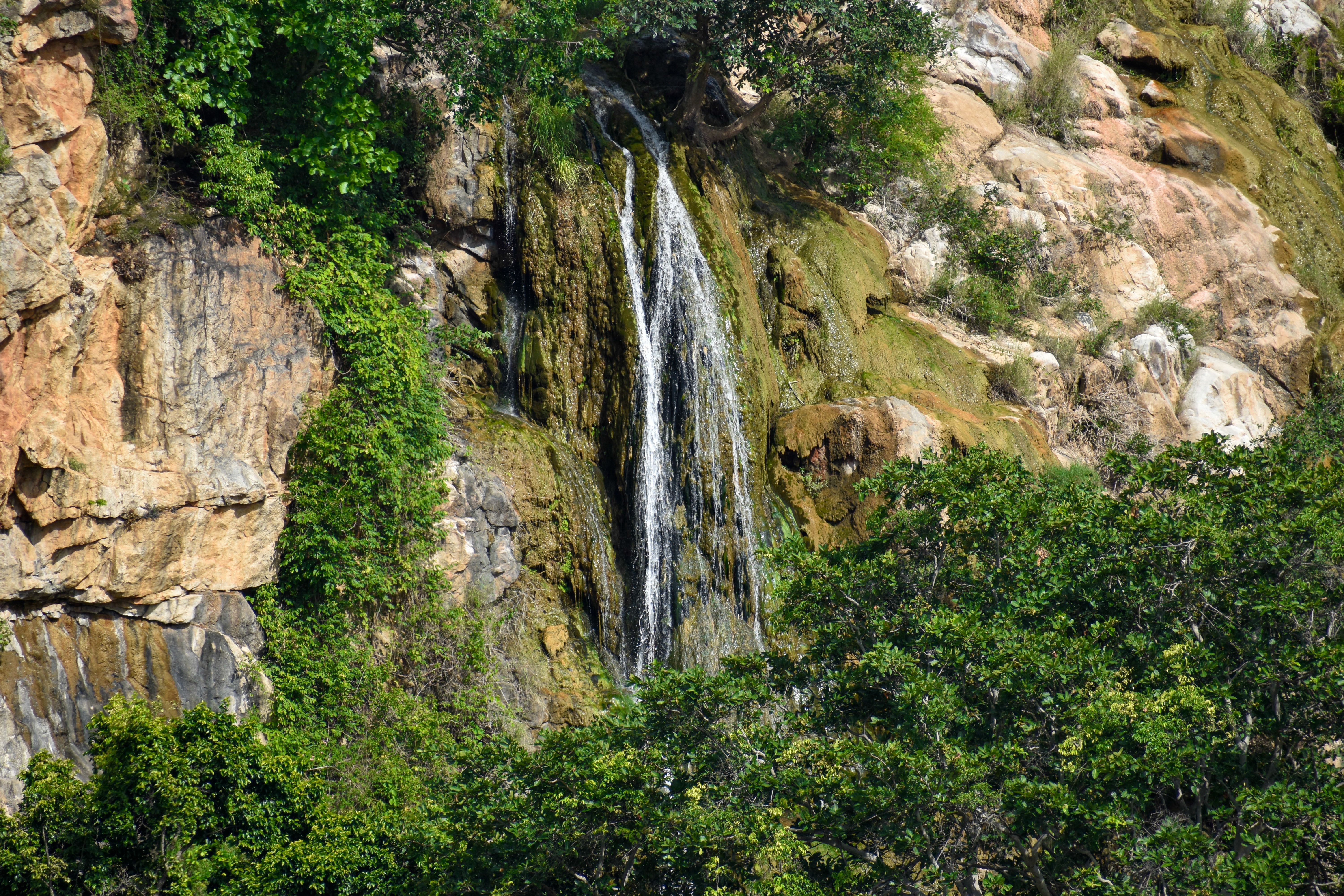 A tranquil waterfall flowing through rocks and green trees in Chamarajnagar, India.
